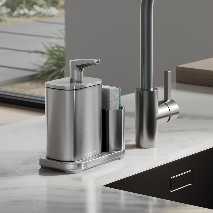 Simplehuman Brushed Pulse Pump with Caddy on kitchen sink edge, sponge in caddy on marble countertop.
