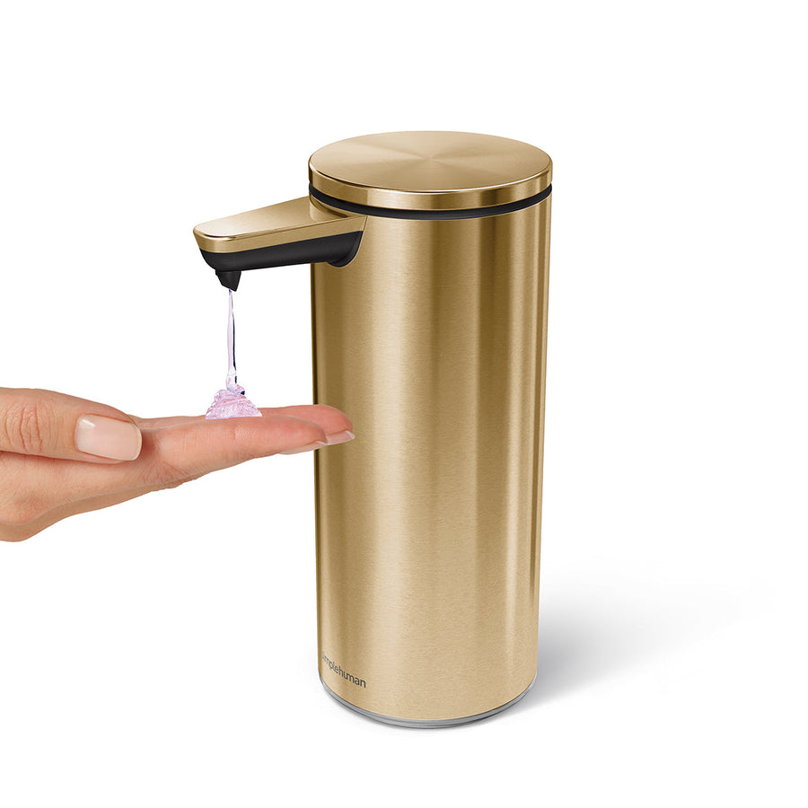 Simplehuman 9 oz. Sensor Pump in Brushed Brass dispensing liquid soap onto a hand, hands-free usage.