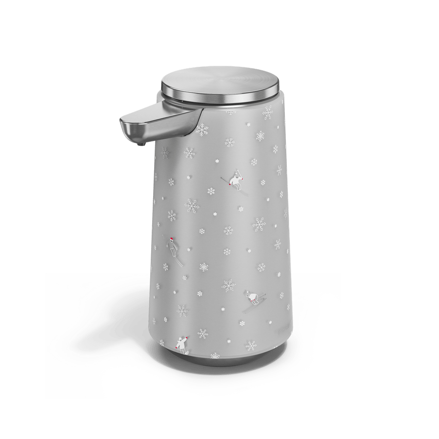 Angled view of Simplehuman Brushed 10 oz. Sensor Pump Foam with holiday sleeve. White, frosted sleeve with skiers and snowflakes. 
