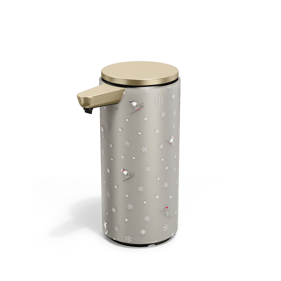 Angled view of Simplehuman Matte Gold 9 oz. Sensor Pump with holiday sleeve. White, frosted sleeve with skiers and snowflakes. 