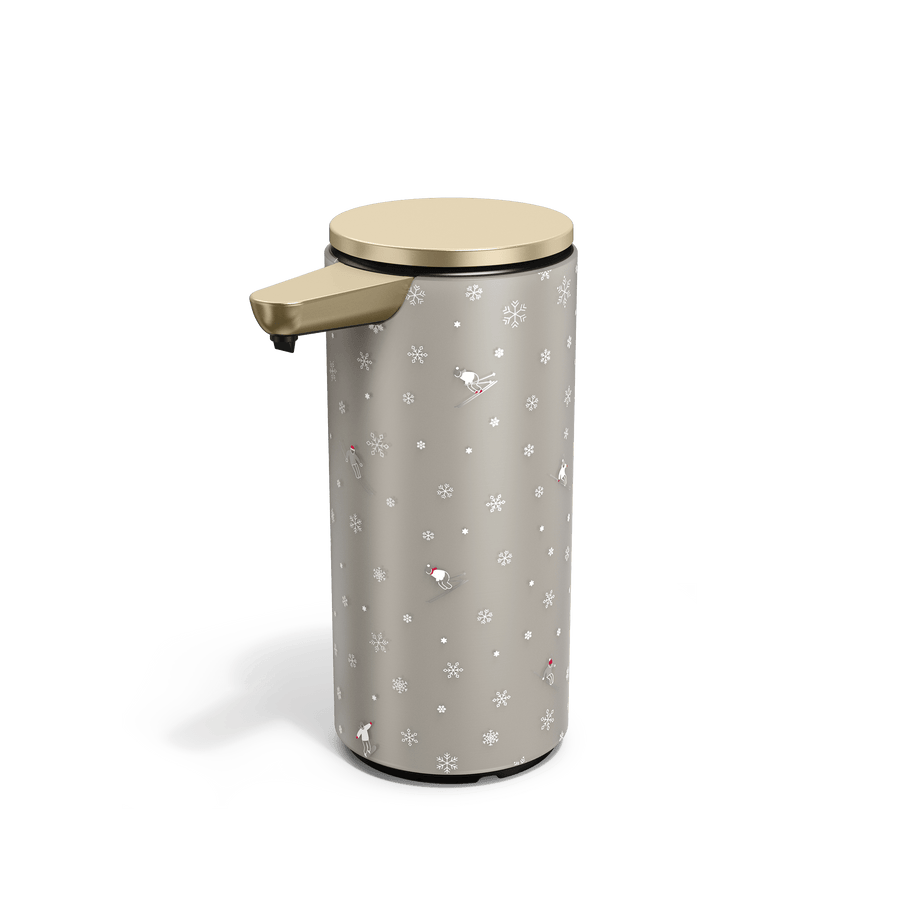 Angled view of Simplehuman Matte Gold 14 oz. Sensor Pump with holiday sleeve. White, frosted sleeve with skiers and snowflakes. 