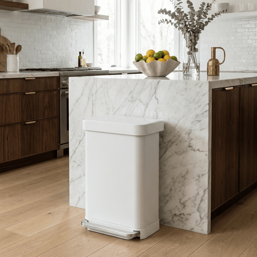 Simplehuman's 55L Step Can in white with in a mid-century modern kitchen setting with white marble countertops and wooden cabinetry.
