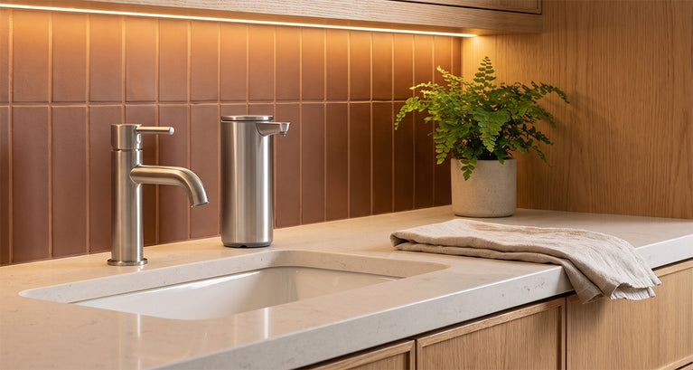 Simplehuman's Liquid Sensor Pump in a rustic home setting with marble countertops, wooden cabinets, and brown tiled backsplash. 