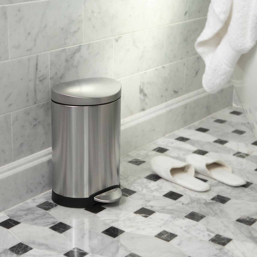 Simplehuman 6L Semi-Round Step Can in Brushed Stainless Steel used in a marble bathroom, space-saving hands-free pedal.